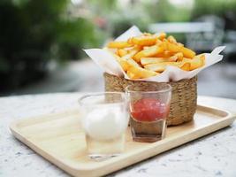 patatine fritte, patatine fritte gialle croccanti nel cestino di legno, spuntino delizioso con salsa di pomodoro e maionese su vassoio di legno foto