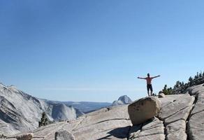 giovane uomo in piedi su una roccia con le braccia alzate davanti a un panorama della catena montuosa dello Yosemite foto