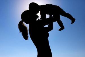 una giovane ragazza tiene in braccio un bambino contro il sole. fotografia di silhouette. foto