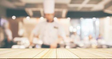 tavolo in legno vuoto con chef che cucina nella cucina del ristorante sfocato sfondo sfocato foto