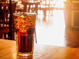 bicchiere di cola con ghiaccio sul tavolo di legno sullo sfondo del ristorante foto