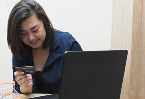 una donna in possesso di una carta di credito, che sta pagando online, si siede sulla sedia nel soggiorno di casa su un laptop. il concetto di shopping online. foto