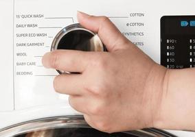 la mano di una casalinga che tiene il controller programmabile giornaliero della lavatrice e mostra i vari programmi di lavaggio. messa a fuoco selettiva. foto