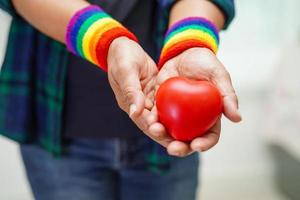 donna asiatica che tiene un hert rosso con bandiera arcobaleno, diritti dei simboli lgbt e uguaglianza di genere, mese dell'orgoglio lgbt a giugno. foto