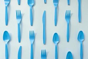 molte forchette, cucchiai e coltelli di plastica blu su sfondo chiaro, vista dall'alto. stoviglie usa e getta, concetto di plastica di smistamento. modello creativo, piatto foto