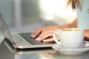 mani di donna digitando in un computer portatile in una caffetteria foto