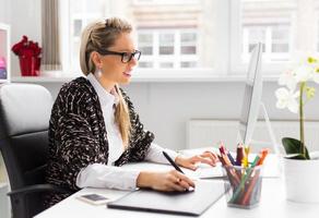 designer femminile che utilizza la tavoletta grafica mentre si lavora con il computer foto
