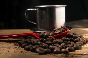 chicchi di caffè sul cucchiaio rosso con sfondo tazza inossidabile foto