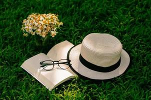 svago in giardino con libro, cappello di paglia e fiori sul prato. foto