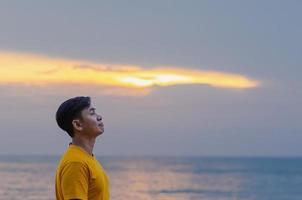uomo asiatico sorridente e alzando lo sguardo con il mare qualsiasi sfondo del cielo. buon concetto di salute mentale. foto