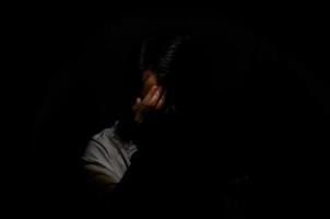 uomo depresso miserabile asiatico seduto da solo su sfondo scuro. concetto di depressione e salute mentale. foto