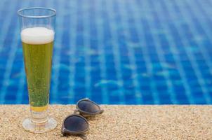 un bicchiere di birra con occhiali da sole messi oltre alla piscina. concetto estivo e rilassante. foto
