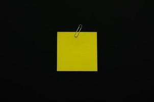 carta per appunti in bianco gialla con graffetta su sfondo scuro. concetto minimalista piatto nero. foto