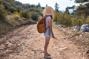 una donna con uno zaino e un cappello di paglia su un sentiero di montagna foto