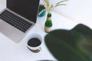 posto di lavoro freelance, laptop, tazza di caffè e pianta in vaso sul tavolo bianco foto