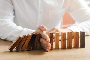 gestione del rischio, la mano dell'uomo d'affari ferma la continua caduta di domino di legno, ferma l'impatto della crisi aziendale. copertura per risolvere i problemi aziendali per il successo. foto