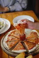 una giovane donna è felice di vedere il cibo in tavola e scegliere il menù della pizza da mangiare con buon gusto. i menù pizza sono perfetti per i banchetti tra amici e familiari in quanto sono comodi da mangiare foto