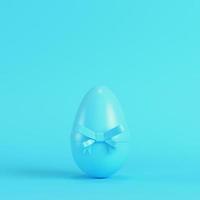 uovo di pasqua con fiocco su sfondo blu brillante in colori pastello foto
