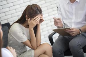 frustrata giovane donna d'affari e infelice tenendo la testa tra le mani durante la sessione di psicoterapia, psichiatra che prende appunti sul diario dell'ufficio di lavoro foto