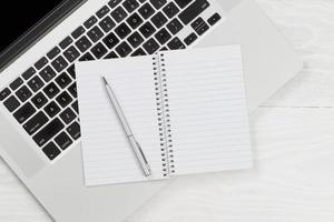 computer portatile con blocco note vuoto e penna sul desktop bianco