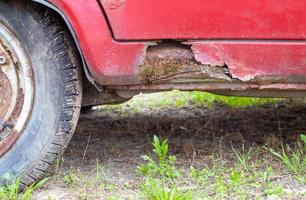 davanzali arrugginiti della porta del guidatore. corrosione della carrozzeria di una vecchia auto rossa dopo l'inverno. influenza dei reagenti in inverno sulla carrozzeria del veicolo non protetta. danneggiamento sul lato sinistro, soglia marcia in basso. foto