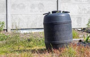 grande fusto di plastica nera con acqua nel giardino estivo. serbatoio dell'acqua piovana in giardino, calda giornata estiva. botti per innaffiare il giardino. foto