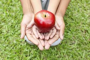 mani adulte che tengono le mani del bambino con la mela rossa foto