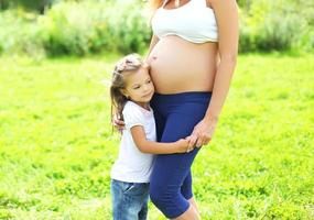 donna incinta felice, la figlia del piccolo bambino ascolta la madre della pancia