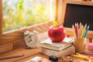 mela posta su un libro con attrezzature educative vicino alla finestra alla luce del mattino, concetto di ritorno a scuola e spazio per la copia foto