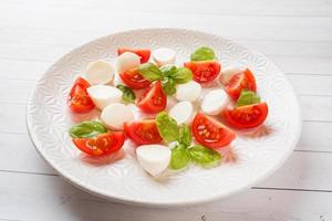 insalata caprese di pomodori, mozzarella e basilico su un piatto bianco. cucina italiana. foto
