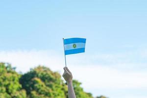 mano che tiene la bandiera dell'argentina sullo sfondo della natura. 9 luglio del giorno dell'indipendenza, 25 maggio del giorno della rivoluzione e felici concetti di celebrazione foto