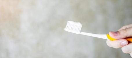 mano che tiene spazzolini da denti con dentifricio in bagno. stile di vita, routine quotidiana, giornata mondiale della salute orale e concetto di giornata dentale gratuita foto