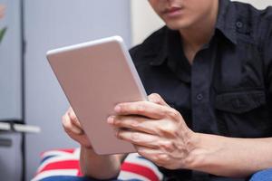 uomo asiatico in camicia nera gioca il suo tablet PC foto
