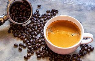 tazza bianca di caffè americano con una bella crema in cima su un tavolo di cemento vicino a un portafiltro con chicchi di caffè arabica. concentrarsi su una tazza di caffè foto