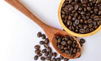 vista dall'alto del chicco di caffè biologico tostato marrone scuro in una ciotola di legno e cucchiaio su sfondo bianco. messa a fuoco selettiva sui chicchi di caffè in una ciotola foto