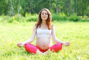 giovane donna incinta seduta sull'erba facendo esercizio di yoga