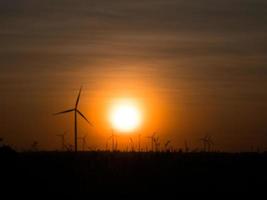 silhouette sfocata turbina eolica e campo in erba con il tramonto foto