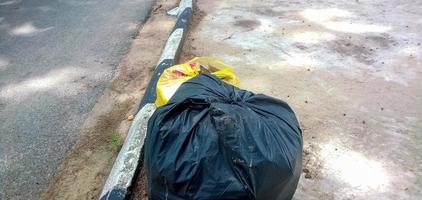 2 borse da garage di plastica sono vicino alla strada asfaltata. il colore di questo sacco della spazzatura di plastica è nero e giallo. foto