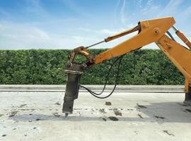 escavatore che rompe e perfora la strada di cemento per la riparazione. grande martello pneumatico montato sul braccio idraulico di un'attrezzatura da costruzione. veicoli da costruzione che riparano strada. martello pneumatico perforato foto