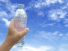 mano dell'uomo che tiene una bottiglia di plastica di acqua e sfondo del cielo foto