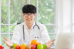 Ritratto di un nutrizionista maschio asiatico sorridente con frutti biologici freschi sani nel suo concetto di ufficio, assistenza sanitaria e dieta foto