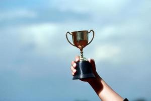 un successo vincitore che celebra con il premio del trofeo e il concetto di campione, tenendo a mano il trofeo del campionato contro il cielo blu. foto