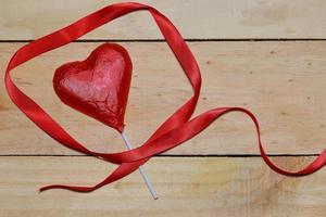 cuore di cioccolato avvolto in nastro rosso e rosso su legno. concetto di San Valentino. spazio per il testo. foto