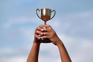 un successo vincitore che celebra con il premio del trofeo e il concetto di campione, tenendo a mano il trofeo del campionato contro il cielo blu. foto