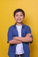 felice giovane ragazzo asiatico in stile denim casual con le braccia incrociate isolate su sfondo giallo foto