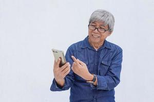 ritratto di uomo anziano asiatico in stile casual denim che indica il dito verso lo smartphone. stile di vita e concetto senior online e social network foto