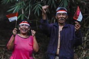 coppia anziana indonesiana che celebra insieme il giorno dell'indipendenza dell'indonesia al villaggio. vecchio e donna che usano una fascia rossa e bianca e tengono una piccola bandiera indonesiana. foto