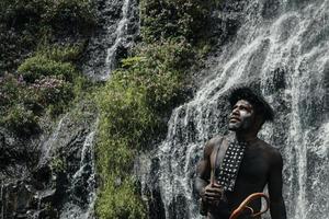 Papua uomo della tribù dani in piedi e guardando in alto, contro la cascata nella foresta verde. foto