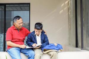 il ragazzo asiatico in uniforme sta seriamente imparando con suo nonno nel cortile di casa. il nonno insegna al nipote. concetto di attività genitoriale e familiare. foto