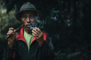 primo piano di un agricoltore asiatico l'uomo anziano sta fumando mentre trasporta la zappa dopo il lavoro sul campo foto